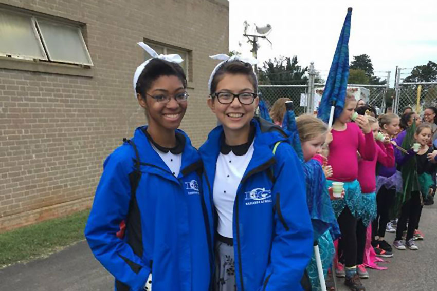 Two marching band students smiling with elementary color guard members in the background