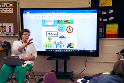 Teacher with logo options on interactive display in background