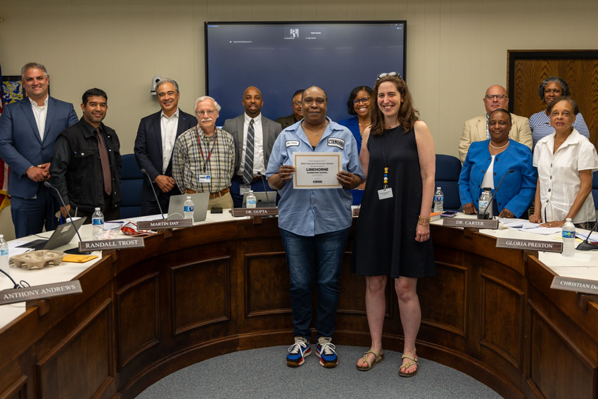 Custodian holding certificate with principal at School Board meeting