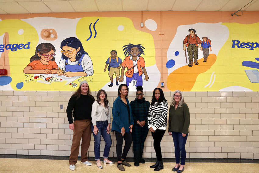 School staff, artist and community members in front of school mural